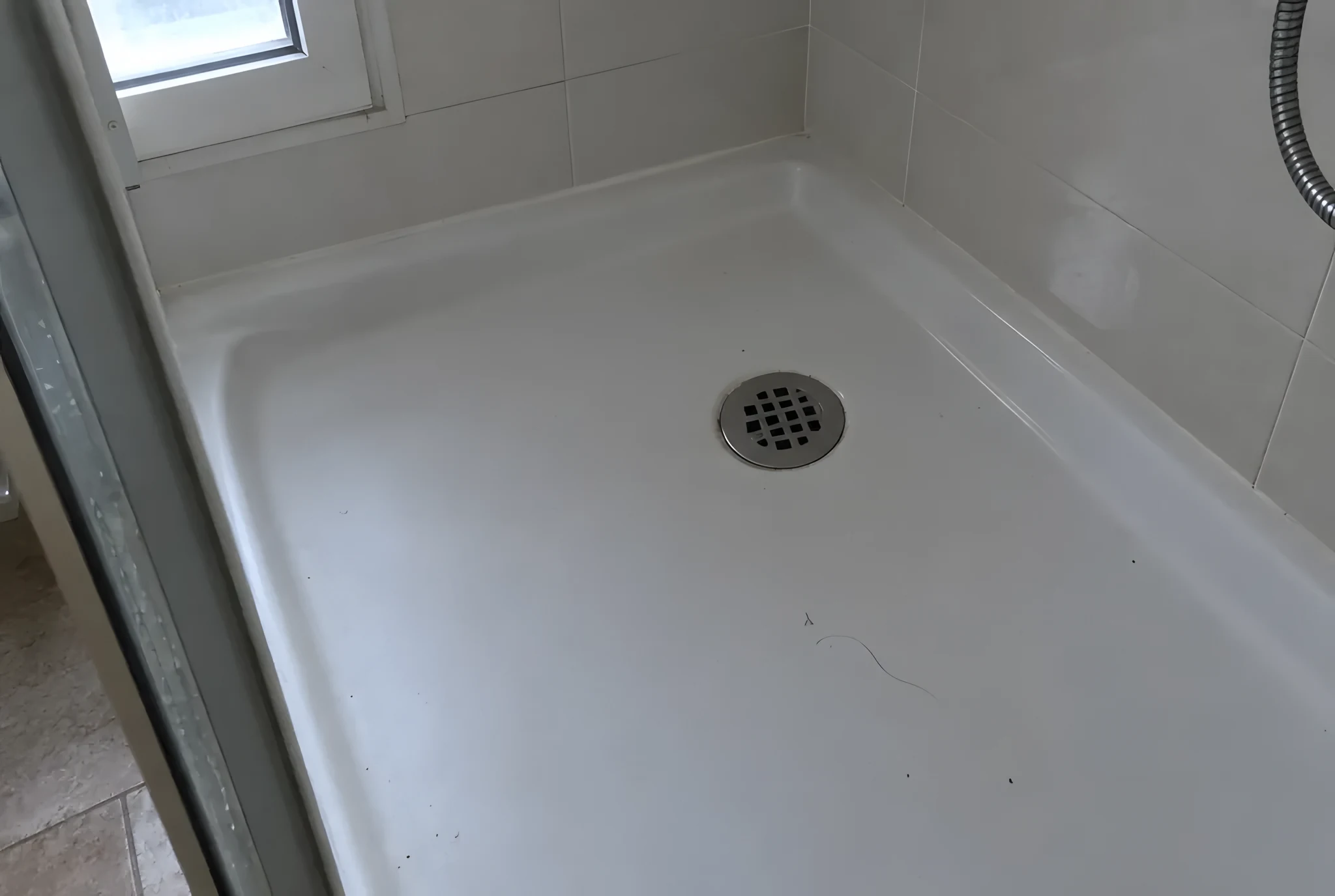Plato de ducha blanco con el sumidero seco y algo de polvo en un baño de invitados