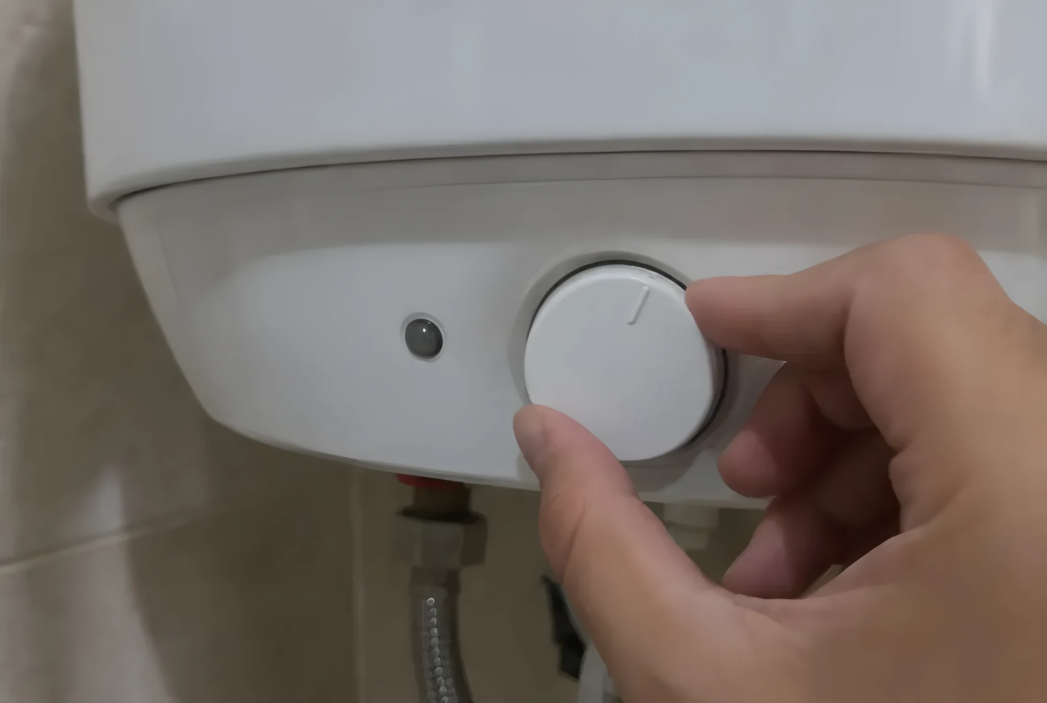 Dedos girando el mando redondo de temperatura en la parte inferior de un termo eléctrico blanco, con el piloto apagado al lado